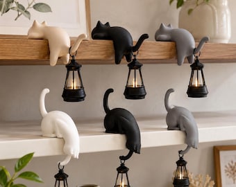 Könnte beinhalten: Sechs katzenförmige Figuren in Weiß, Schwarz und Grau, die jeweils eine kleine schwarze Laterne mit leuchtendem Licht halten. Drei Katzen sind am Rand eines Holzregals positioniert, während drei weitere auf einem weißen Regal sitzen.