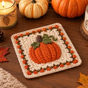 Könnte beinhalten: Ein quadratischer Häkeluntersetzer mit einem zentralen orangefarbenen Kürbis mit braunem Stiel und grünen Blättern auf cremefarbenem Grund. Der Rand ist mit einem sich wiederholenden Muster aus kleinen orangefarbenen Kürbissen und grünen Ranken verziert.