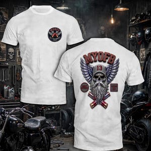 May include: A white short-sleeve t-shirt featuring a small circular logo on the left chest and a large graphic on the back. The back graphic displays a skull with a beard, sunglasses, and a cap with the number 13, flanked by wings and crossed shotgun shells.