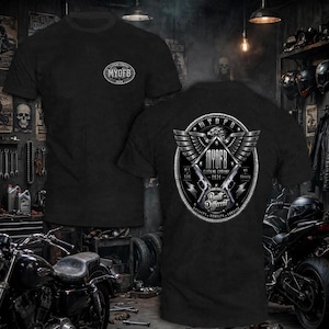 May include: A black short-sleeved t-shirt featuring a small oval logo on the front chest that reads MYOFB 2026. The back displays a large circular graphic with an eagle, two crossed pistols, and the text MYOFB CLOTHING COMPANY 2026 BUILT DIFFERENT.