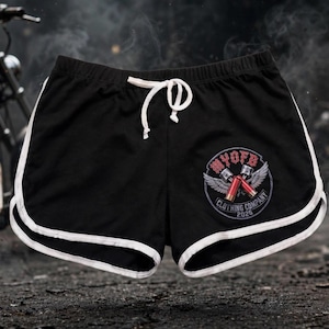 Könnte beinhalten: Schwarze Sportshorts mit weißem Saum entlang des geschwungenen Beinabschlusses und einem weißen Kordelzug am elastischen Bund. Ein kreisförmiges Motiv auf dem rechten Bein zeigt den Text MYOFB CLOTHING COMPANY 2023 mit zwei gekreuzten Kolben.