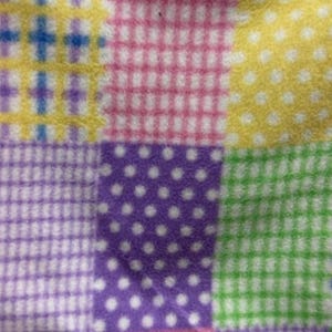 May include: A fabric featuring a patchwork design with alternating squares of green and white gingham, yellow and white polka dots, purple and white polka dots, and a white background printed with small pink and blue flowers with yellow centers.