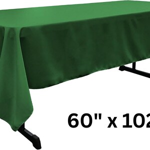 May include: A solid forest green rectangular tablecloth draped over a black folding table. The fabric has a smooth, matte finish and hangs down on all sides. The text 60" x 102" is printed in black in the lower right corner of the image.