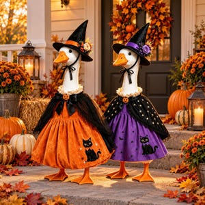 May include: Two white goose figurines dressed in Halloween costumes. One wears an orange velvet dress with a black cat print and a black witch hat. The other wears a purple dress with a black cat print, a star-patterned cape, and a black witch hat.