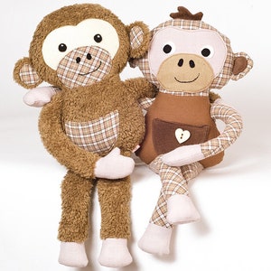May include: Two plush monkey toys sitting side-by-side. The monkey on the left is brown with a plaid pocket and pink feet. The monkey on the right is brown and white plaid with a brown pocket and pink feet.