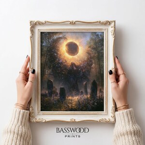 May include: A framed wall art print featuring a celestial scene with a dark moon surrounded by a golden sunburst glow above a forest clearing with standing stones and purple wildflowers. The frame is ornate, off-white with gold trim accents.