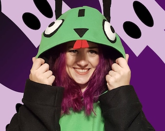 May include: A green hooded sweatshirt with black sleeves. The hood is designed to resemble a cartoon character with white eyes, black ears, and a red tongue. The person is smiling and holding the hood.