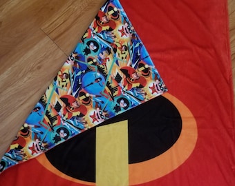 May include: A red blanket with a large black oval and yellow stripe design. The blanket is folded to reveal a patterned fabric with cartoon characters in blue, orange, and yellow. The blanket is rectangular.
