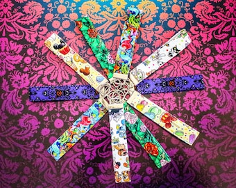 May include: A collection of colorful lanyards with various themed patterns, including cartoon characters, roses, and abstract designs. The lanyards are arranged in a circular pattern around a silver metal centerpiece, set against a patterned background.