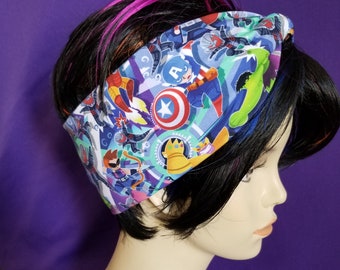 May include: A colorful headband featuring a repeating pattern of comic book characters, including Captain America and the Hulk, on a blue, green, and purple background. The headband is worn on a mannequin head with black hair and pink highlights.