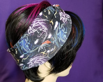 May include: A black fabric headband featuring a dragon pattern in white, blue, orange, and yellow. The headband is knotted at the top and worn on a mannequin head with black hair and streaks of pink, blue, and orange.