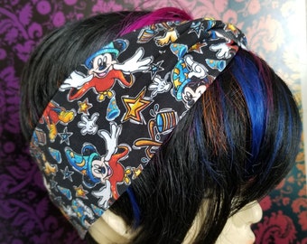 May include: Black headband featuring a repeating pattern of Mickey Mouse in various poses, stars, and other cartoon elements. The headband is worn on a person with black hair and colorful streaks.