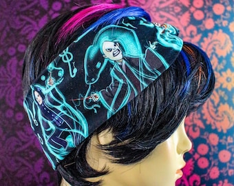 May include: Black headband featuring a repeating pattern of a wizard and a snake in teal and white. The headband is worn on a mannequin with black hair and pink and blue highlights. The background is a floral pattern.