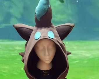 May include: Brown hooded sweatshirt with a character-themed design. The hood features a character's face with blue accents and ears. The sweatshirt has a faux fur collar and blue cuffs. A pocket is visible on the front.