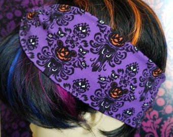 May include: A purple headband with a Halloween-themed pattern featuring black silhouettes of haunted house designs, Mickey Mouse jack-o'-lanterns, and spooky eyes. The headband is worn on a mannequin head with black, orange, blue, and pink hair.