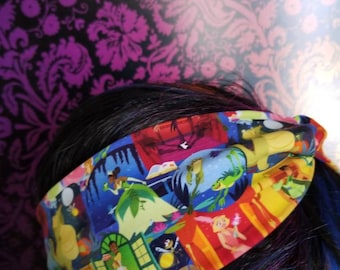 May include: A colorful headband featuring a collage of cartoon characters in various scenes. The headband is primarily yellow, red, and blue, with images of animated characters. The headband is worn on a person's head.