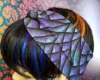 May include: A wide headband with a geometric pattern in shades of purple, black, and teal. The fabric has a textured appearance, and the headband is worn on a mannequin head with dark hair and colorful streaks.