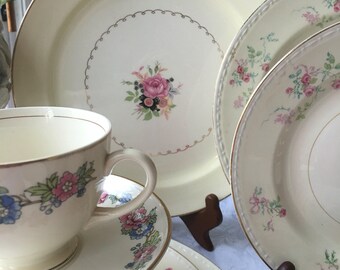 May include: A set of vintage floral china plates and a teacup and saucer. The plates have a delicate floral pattern with pink and green accents. The teacup and saucer have a similar floral pattern with blue and pink accents.