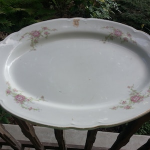 May include: White oval serving platter with a gold rim and delicate pink floral design.