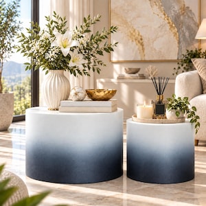 May include: A set of two cylindrical side tables featuring a smooth gradient finish that transitions from white at the top to a deep navy blue at the base. The tables have a solid, drum-like structure with a clean, minimalist silhouette.