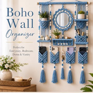 May include: A blue macrame wall organizer featuring a central circular mirror, multiple shelves, and four pockets for mobile devices. The piece is accented with white and blue beads, hanging tassels, and includes text reading Boho Wall Organizer.