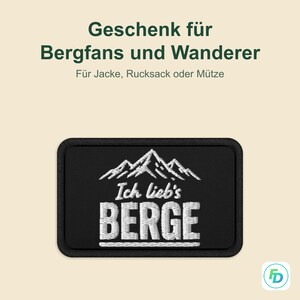 Könnte beinhalten: Ein rechteckiger, schwarzer Aufnäher mit weißer Berg-Stickerei und dem deutschen Text Ich lieb's BERGE. Der Hintergrundtext lautet Geschenk für Bergfans und Wanderer, Für Jacke, Rucksack oder Mütze, mit einem kleinen Logo in der Ecke.