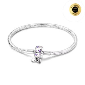 Può includere: Un bracciale a catena snake in argento con un singolo charm cilindrico. Il charm è decorato con piccoli motivi a farfalla viola e accenti circolari. Un piccolo charm a farfalla in argento pendente è fissato alla base della perla principale.