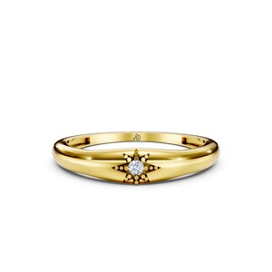 May include: A polished yellow gold band ring featuring a central starburst motif with a single round clear gemstone at its center. The interior of the band displays a small engraved logo consisting of the letters A and J intertwined in a script font.