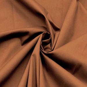 Peut inclure: Un tissu brun moyen uni avec une texture lisse et mate. Le matériau est drapé en spirale centrale, créant des plis profonds et doux ainsi que des ombres qui soulignent la couleur brune terreuse et uniforme sur toute la surface du textile.