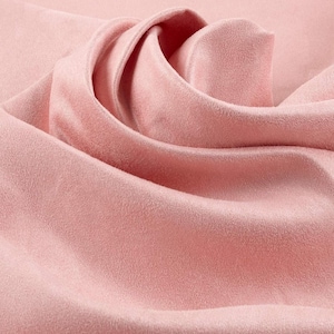May include: A soft, light pink fabric with a matte, suede-like texture. The material is draped in gentle, flowing folds, creating deep shadows and highlights that emphasize the smooth, uniform surface and the consistent pastel pink color throughout.