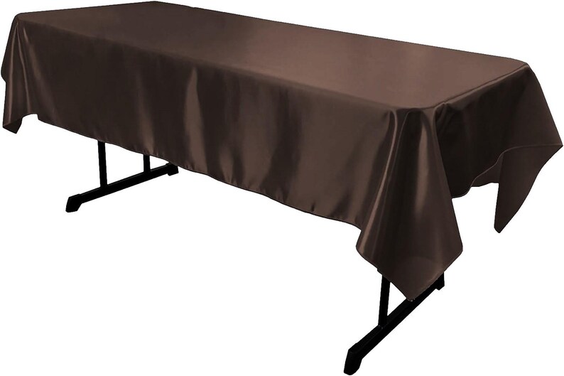 May include: A rectangular table covered with a solid dark brown satin tablecloth. The fabric has a smooth, reflective finish and drapes over the edges of the black folding table frame, which features thin metal legs and a horizontal support bar.