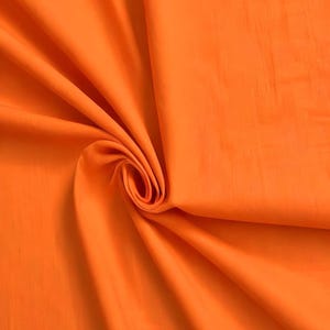 Peut inclure: Un tissu orange vif présentant une texture lisse et mate. Le matériau est drapé en un tourbillon central, créant des plis doux et fluides ainsi que des ombres profondes qui soulignent la couleur unie et constante sur toute la surface du textile.