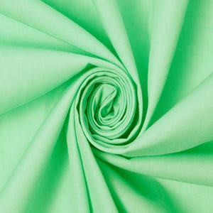 Puede incluir: Una tela de color verde claro sólido con una textura suave, dispuesta en un patrón de espiral central que crea pliegues profundos y radiantes, así como sombras en la superficie, resaltando el color uniforme y el acabado mate del material.