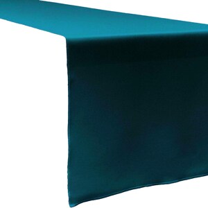 May include: A long, rectangular table runner in a solid, deep teal colour. The fabric has a smooth, slightly reflective finish with clean, straight edges and a hemmed border, draped to show a flat top section and a vertical hanging end piece.