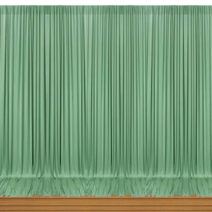 May include: A floor-to-ceiling sage green curtain featuring uniform vertical pleats that create a consistent, draped texture across the entire width. The fabric hangs straight down, ending just above a horizontal wooden surface at the base.