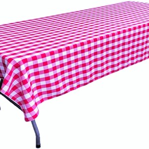 May include: A rectangular folding table covered with a vibrant red and white checkered tablecloth. The fabric features a classic gingham pattern with alternating square blocks of color that drape over the edges of the table frame.