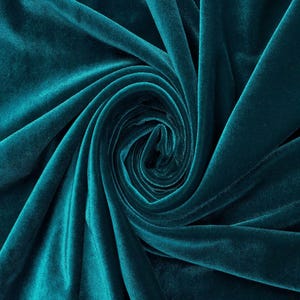 May include: A deep teal velvet fabric featuring a dense, soft pile with a subtle sheen. The material is arranged in a central spiral swirl, creating natural folds and shadows that highlight the rich, saturated color and smooth texture of the textile.