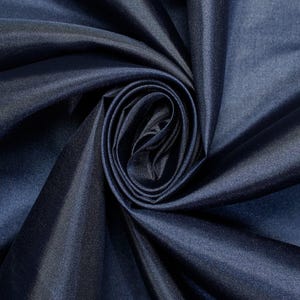 May include: A deep navy blue fabric with a smooth, lustrous finish. The material is arranged in a tight, circular spiral fold, creating soft, flowing drapes and shadows that highlight the reflective quality of the dark blue textile surface.