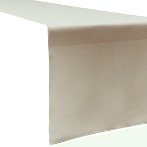 May include: A long, rectangular table runner in a solid, light beige color. The fabric has a smooth, matte texture with clean, straight edges and a finished hem along the sides, draped to show a flat top surface and a vertical hanging end.