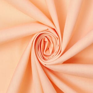 May include: A solid light peach coloured fabric arranged in a tight spiral swirl pattern. The textile features a smooth, matte surface with soft, radiating folds that create depth and shadow, highlighting the consistent pastel orange hue throughout.