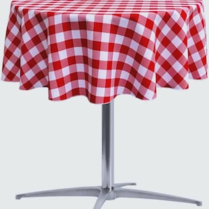 May include: A round table covered with a red and white checkered tablecloth. The table features a single central silver-colored metal pedestal base that branches out into four feet at the bottom, providing a stable support for the circular top.