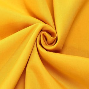 Könnte beinhalten: Ein einfarbiger senfgelber Stoff mit einer glatten, matten Textur. Das Material ist zu einer zentralen Spirale gerafft, wodurch tiefe, fließende Falten und Schatten entstehen, die die gleichmäßige Farbe und das feine Gewebe betonen.