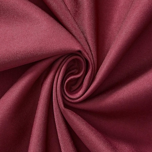 May include: A deep burgundy fabric with a distinct diagonal twill weave pattern. The material is gathered into a central spiral swirl, creating soft, radiating folds and shadows that highlight the smooth, slightly lustrous texture of the textile.
