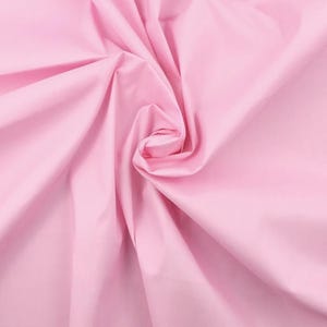 Puede incluir: Una tela de color rosa claro sólido con una textura suave y mate. El material está recogido en el centro, creando pliegues suaves y fluidos y sombras profundas que irradian hacia afuera, resaltando el color rosa pastel uniforme.