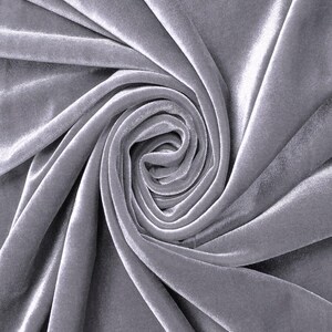 May include: A piece of silver-gray velvet fabric arranged in a spiral pattern. The material features a soft, dense pile with a distinct sheen that creates light and dark highlights across the folds, showcasing the texture of the textile.