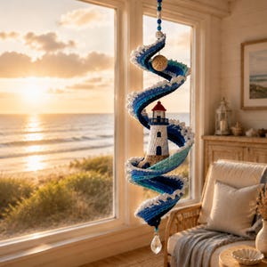 May include: A crocheted spiral hanging decoration featuring a lighthouse in the center, surrounded by waves in shades of blue and white. The structure is suspended from a string of blue beads and terminates in a clear, faceted crystal drop.