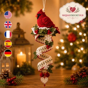 Peut inclure: Une décoration de Noël au crochet représentant un cardinal rouge vif perché sur une branche de houx verte avec des baies rouges. Sous l'oiseau, un ruban torsadé couleur crème est orné de flocons de neige blancs, de feuilles et de baies.