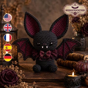 May include: A black and dark red crocheted bat plush toy featuring large pointed ears, two white fangs, and a small dark red bow tie at the neck. The bat has black safety eyes and textured wings with dark red inner detailing, crafted with yarn.