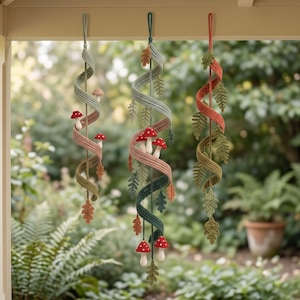 May include: Three hanging spiral decorations made of crocheted yarn. Each piece features a twisted ribbon design adorned with small crocheted mushrooms and various leaf shapes in shades of green, red, orange, and muted pink, suspended by loops.