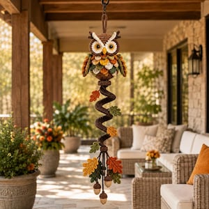 May include: A crocheted owl hanging decoration featuring a brown owl with large yellow eyes, attached to a long, spiraling brown cord adorned with multiple crocheted autumn-colored leaves in shades of orange, yellow, and green, plus small acorns.